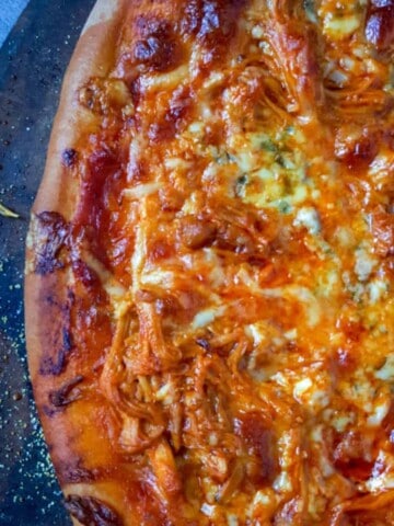 A a close up and partial view of a buffalo chicken pizza on a pizza stone