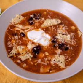 Overhead shot of bowl of chicken tortilla soup with sour cream drizzled on top on a yellow background.