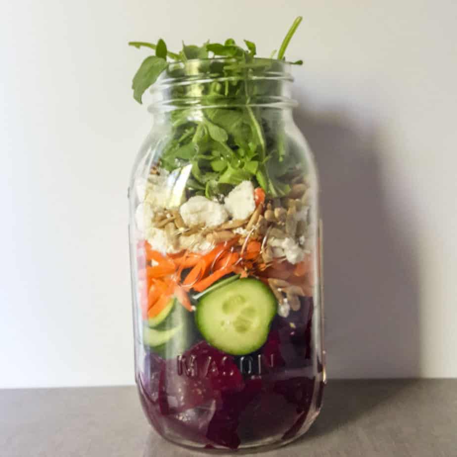  A large mason jar filled with layers of vegetables for a work salad. 