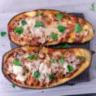 2 halves of eggplant, roasted and stuffed with sausage, pastas sauce and cheese. Topped with parsley in a glass pyrex container. Overhead shot.