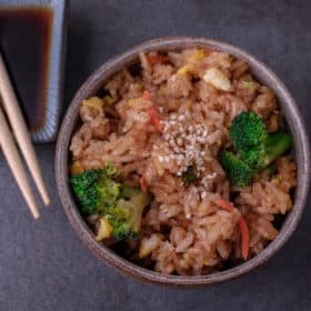 In a small bowl fried rice with chop sticks and soy sauce in the background