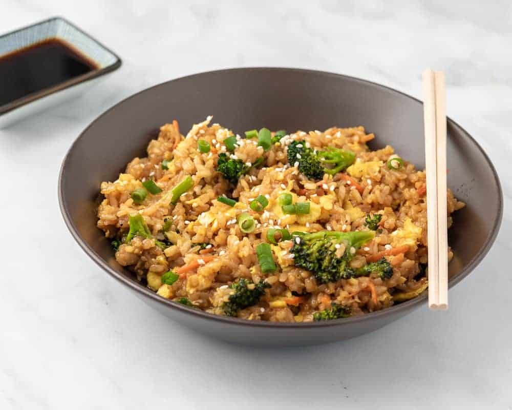 Fried rice in a brown bowl with soy sauce and chopsticks in the background