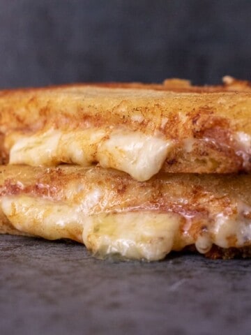 Grilled cheese, cut in half and stacked on top of each other. Cheese is oozing out.