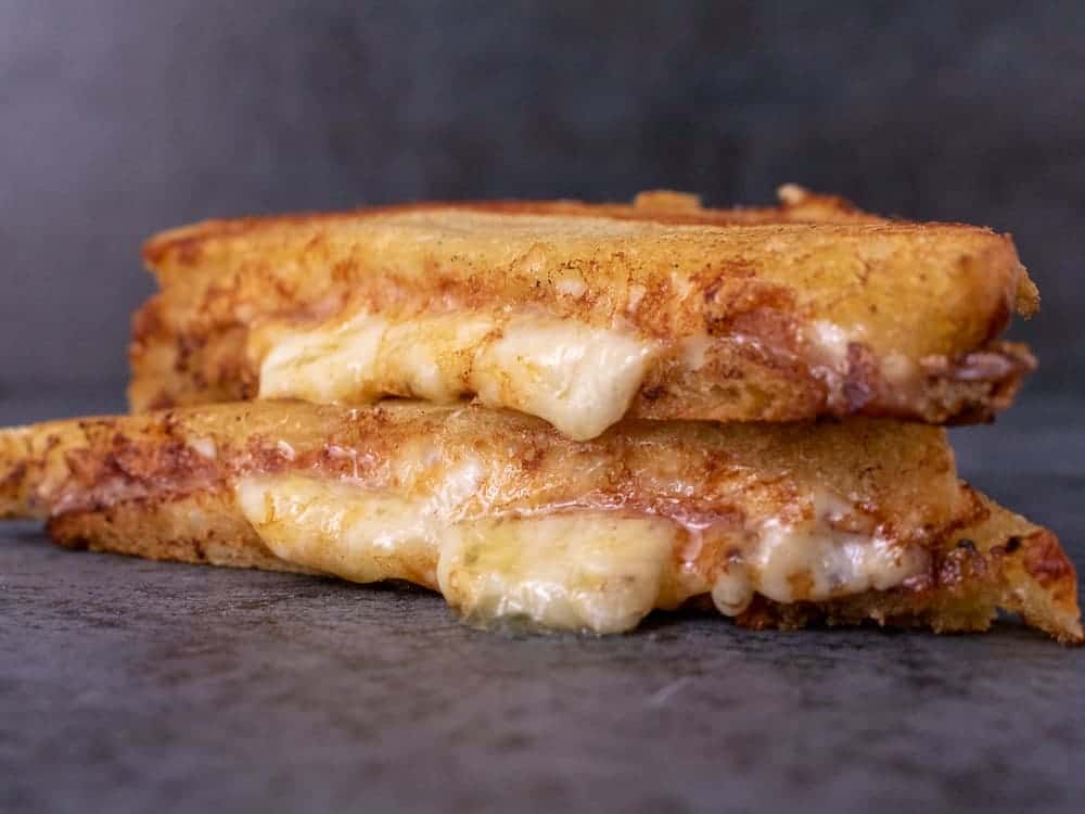 Grilled cheese, cut in half and stacked on top of each other. Cheese is oozing out.