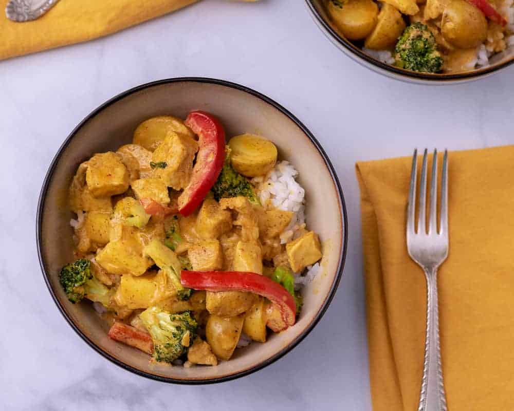 A bowl of yellow curry with chicken, broccoli and red peppers over white rice.