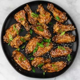 A plate of chicken wings with teriyaki sauce, sesame seeds and scallions.