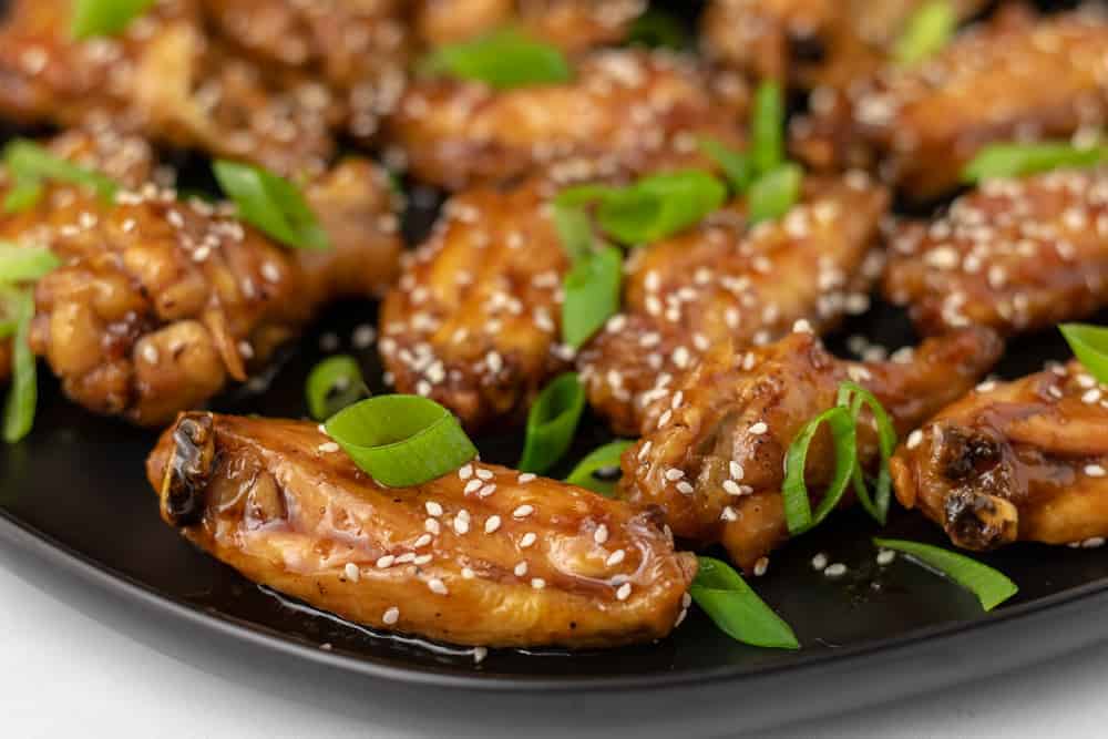 A plate of chicken wings with teriyaki sauce, sesame seeds and scallions.