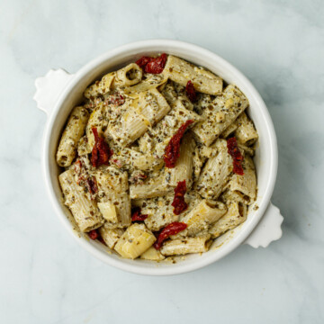 Top down photo of creamy pesto pasta in a white bowl on a white back marble background.