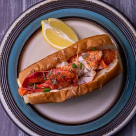 Top down view of a lobster roll in a top split bun with a wedge of lemon