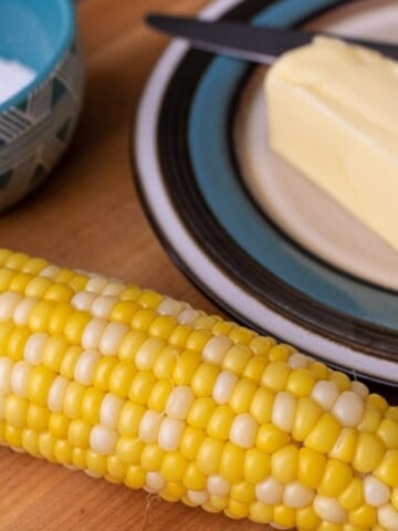 One piece of corn on the cob next to butter and salt.