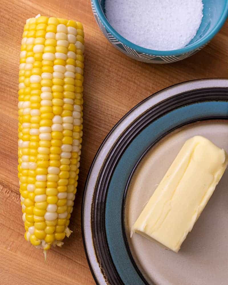 One piece of corn on the cob next to butter and salt.