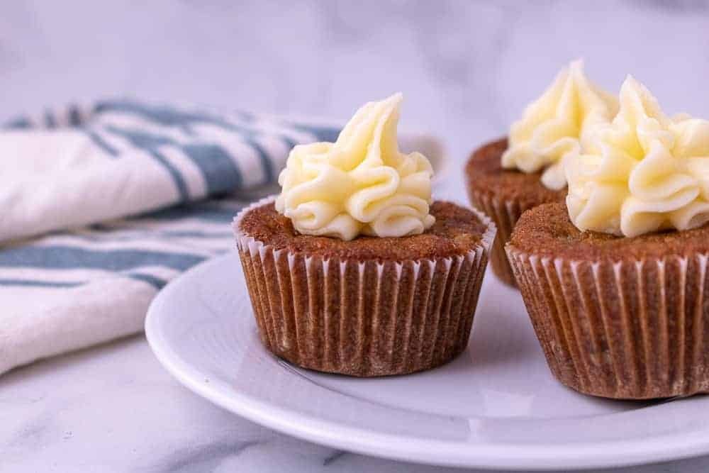 3 Carrot cake cupcakes on a plate with cream cheese frosting