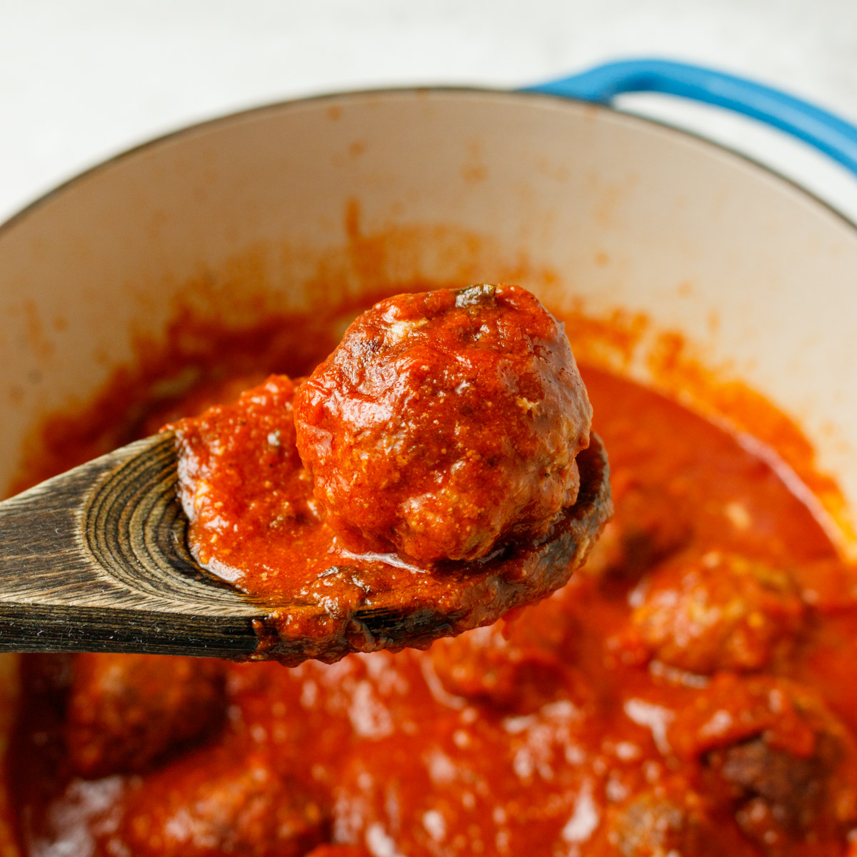 A meatball on a wooden spoon over a dutch oven of meatballs.