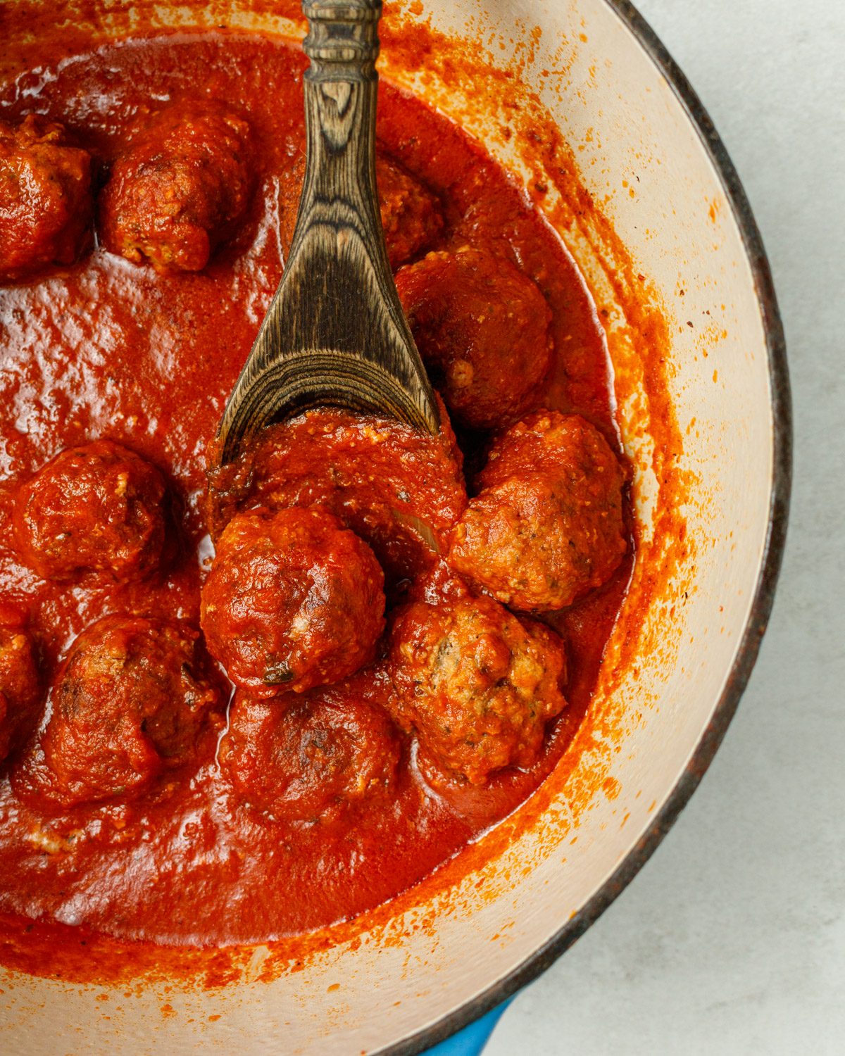 A dutch oven of meatballs in sauce with a wooden spoon