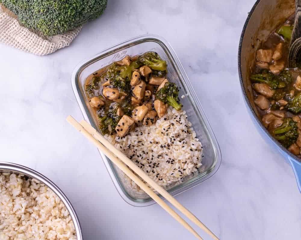 a meal prep container of chicken and broccoli in oyster sauce with broccoli in the background