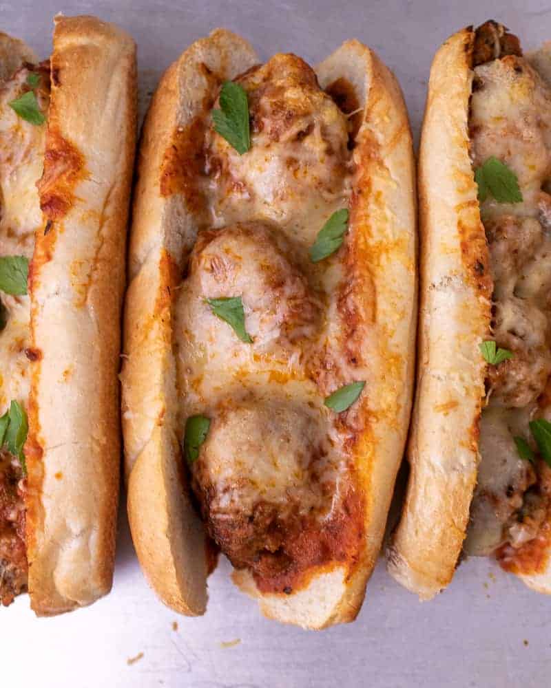 Multiple meatball subs in a row with cheese and parsley