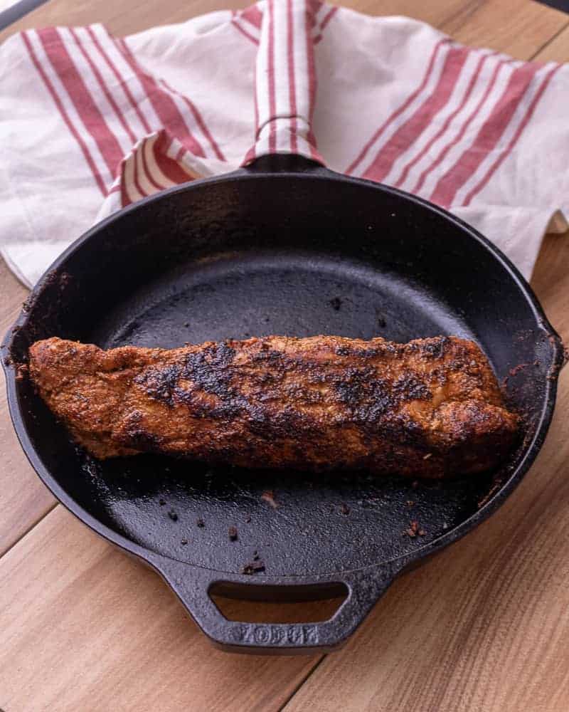 Finished seared cajun pork tenderloin in a cast iron with a napkin over the handle of the pan