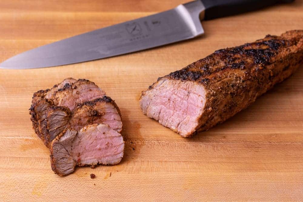 Close up shot of the pork tenderloin being cut by a large chef knife.