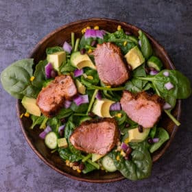 Close up of cajun pork tenderloin spinach salad in a wooden bowl