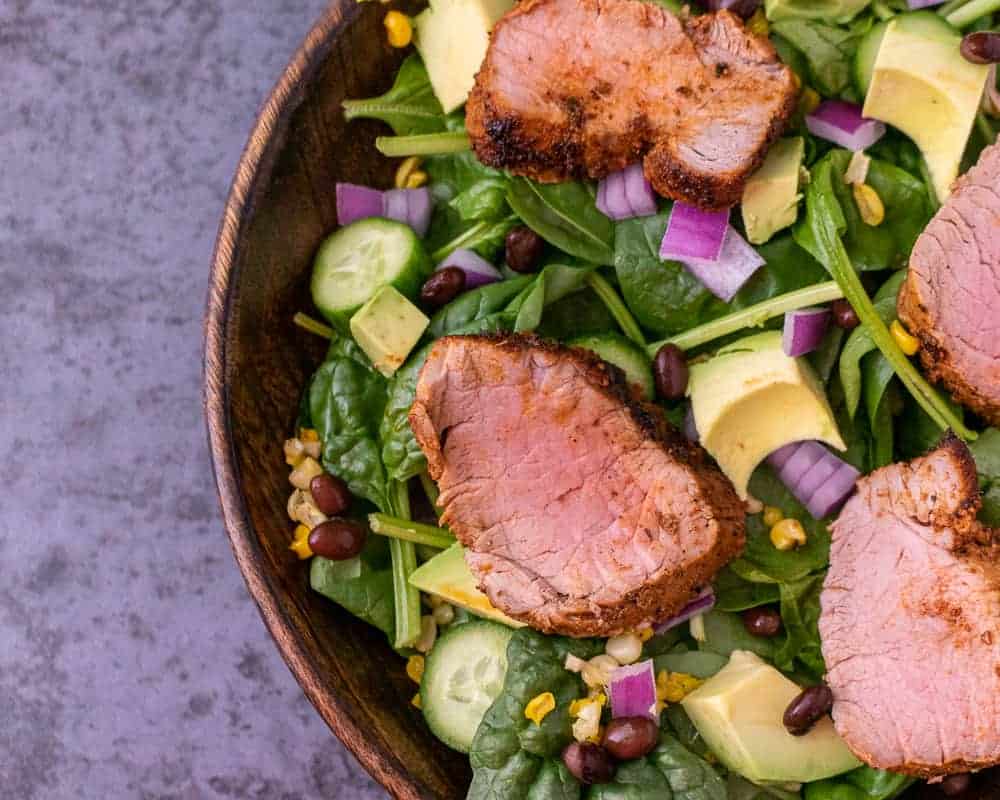 Close up of cajun pork tenderloin spinach salad in a wooden bowl