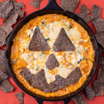 A close up of jack o lantern buffalo chicken dip with black chips around it
