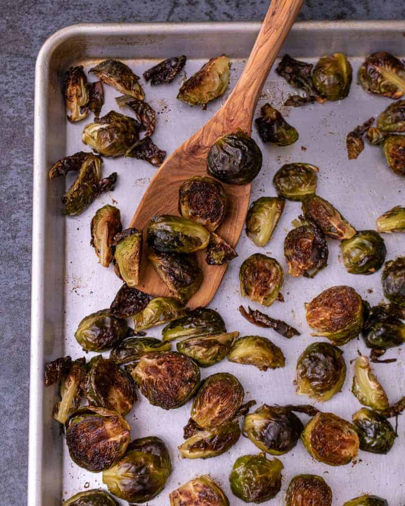 Close up of roasted brussel sprouts on a sheet tray with a wooden spoon