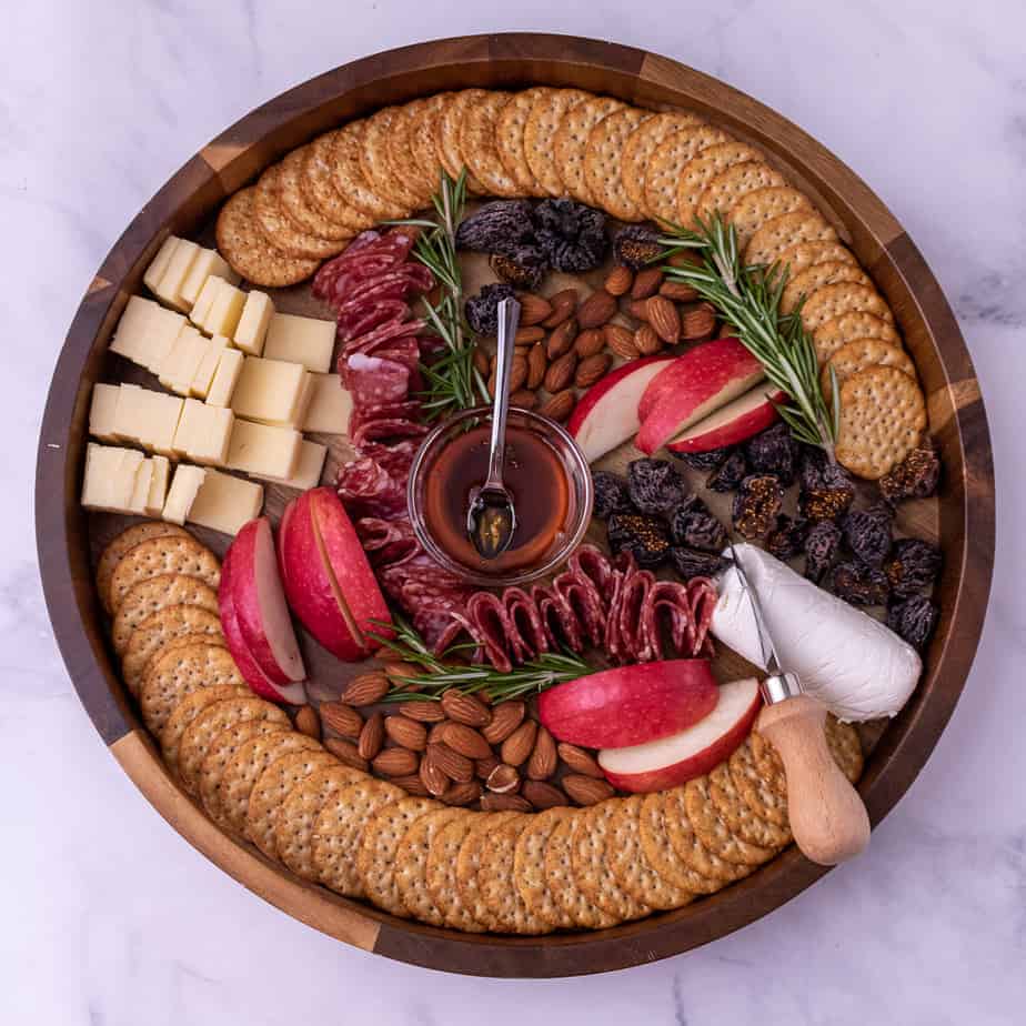 Overhead view of Thanksgiving cheese plate with cheddar cheese, goat cheese, rosemary, crackers, honey, almonds, dried figs and fresh apples