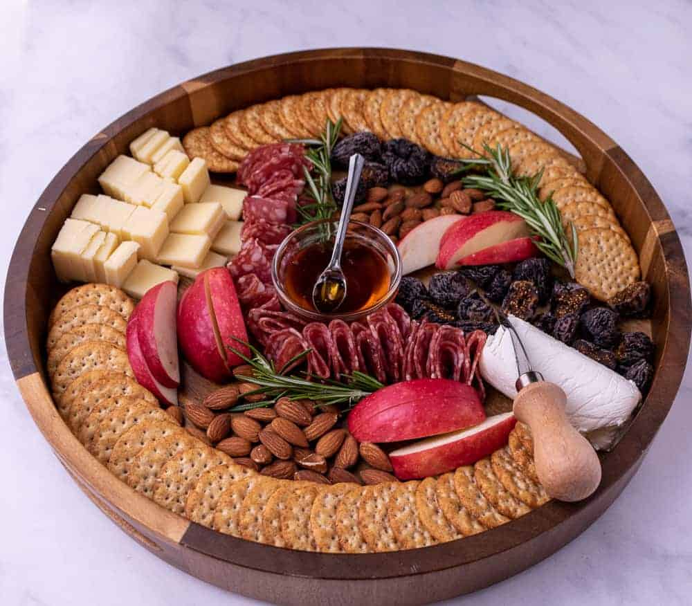 Overhead view of Thanksgiving cheese plate with cheddar cheese, goat cheese, rosemary, crackers, honey, almonds, dried figs and fresh apples