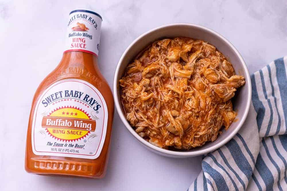 CLose up of shredded buffalo chicken next to a bottle of sweet baby rays buffalo sauce