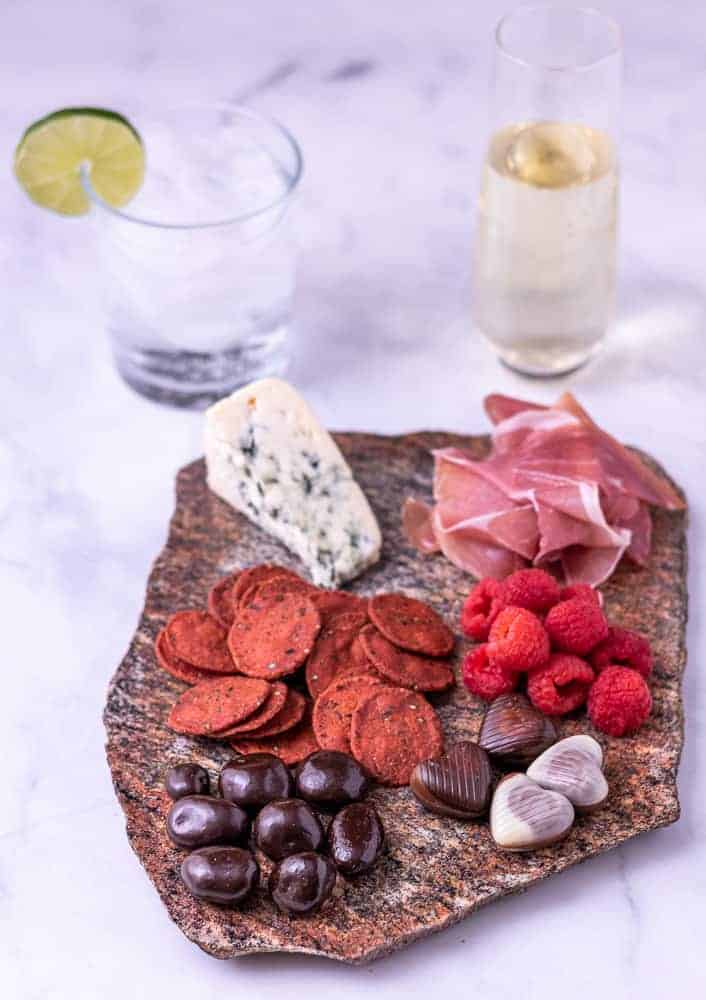 A cheese plate for two with two beverages in the back