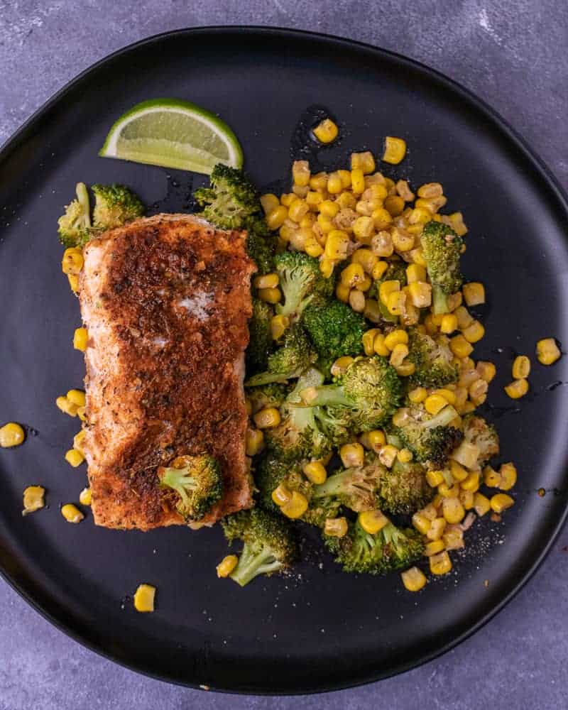 Cooked cajun salmon with veggies on a black plate with a lime wedge