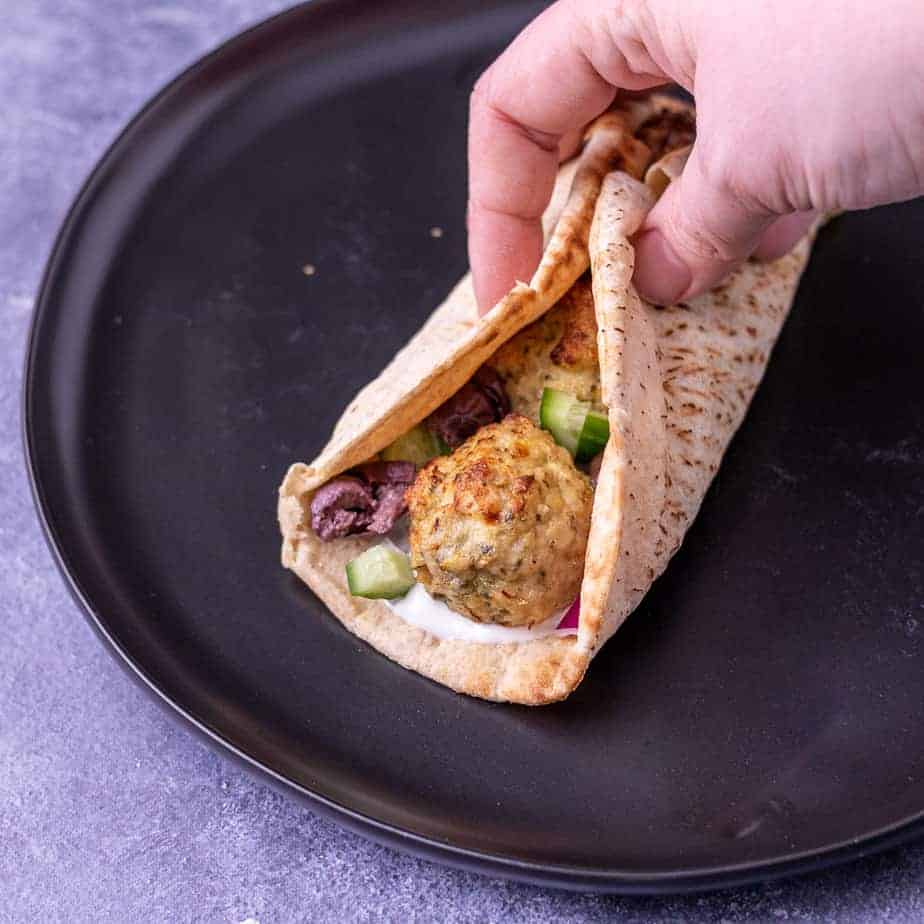 A black plate with a folded up greek meatball pita sandwich