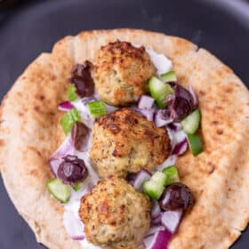 A close up of a meatball pita sandwich with all the toppings.