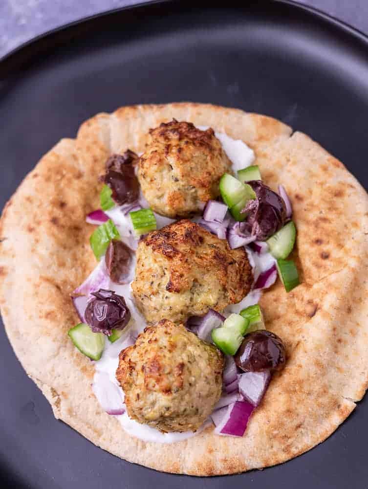 A close up of a meatball pita sandwich with all the toppings.