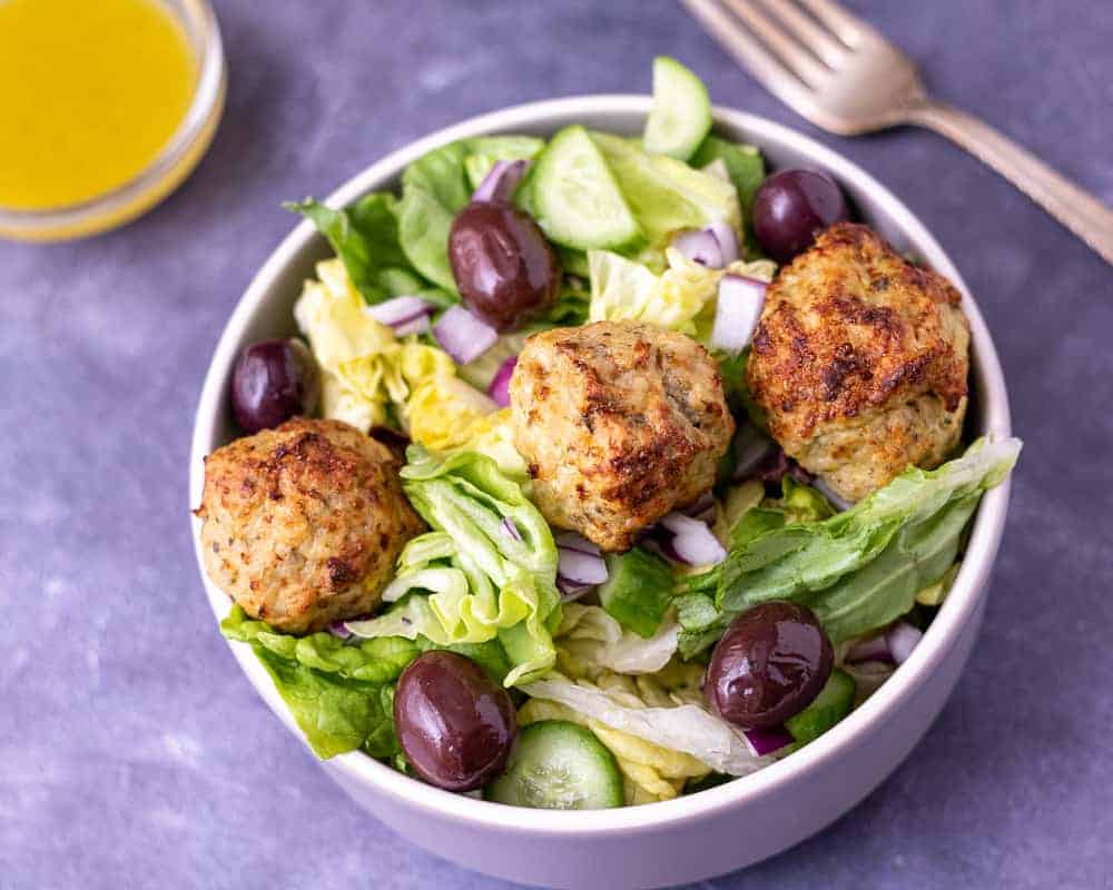 Greek meatball salad in a bowl with a fork and salad dressing