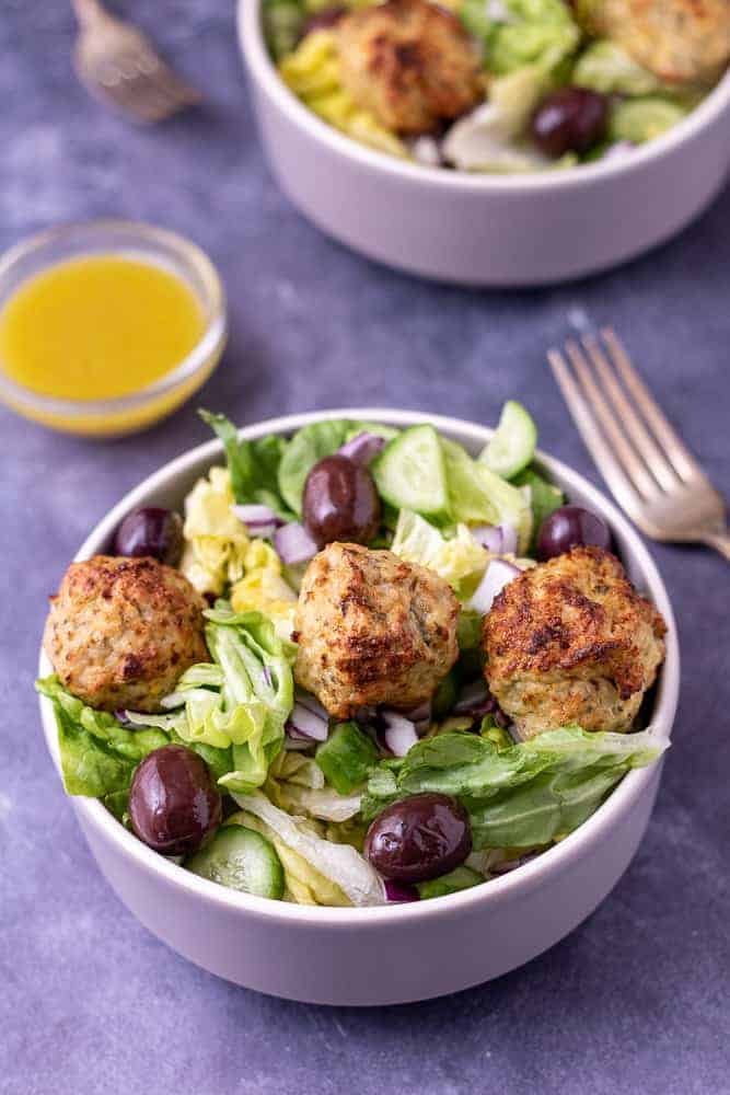 2 bowls of greek chicken salad with forks and salad dressing.