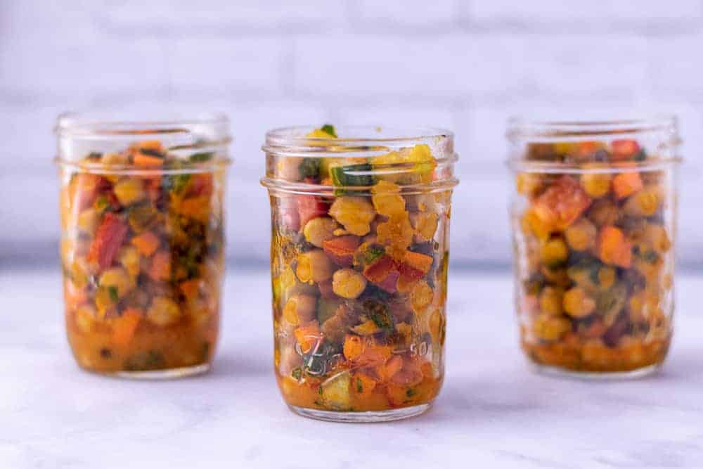 3 mason jars full of chickpea salad in a row in front of a white background.