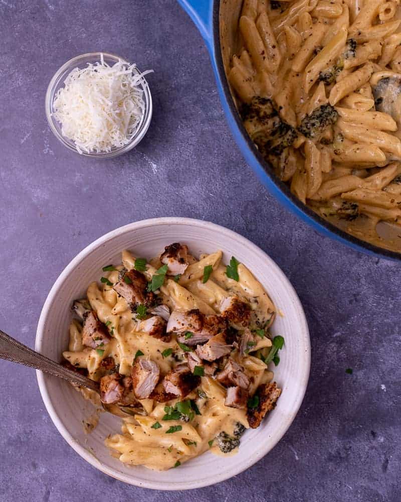 A fully garnished bowl of pasta next to a dutch oven pot full of cooked pasta