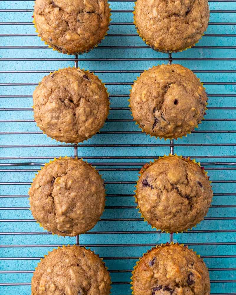 Cooked muffins in two parallel rows on a wire rack on a blue background.