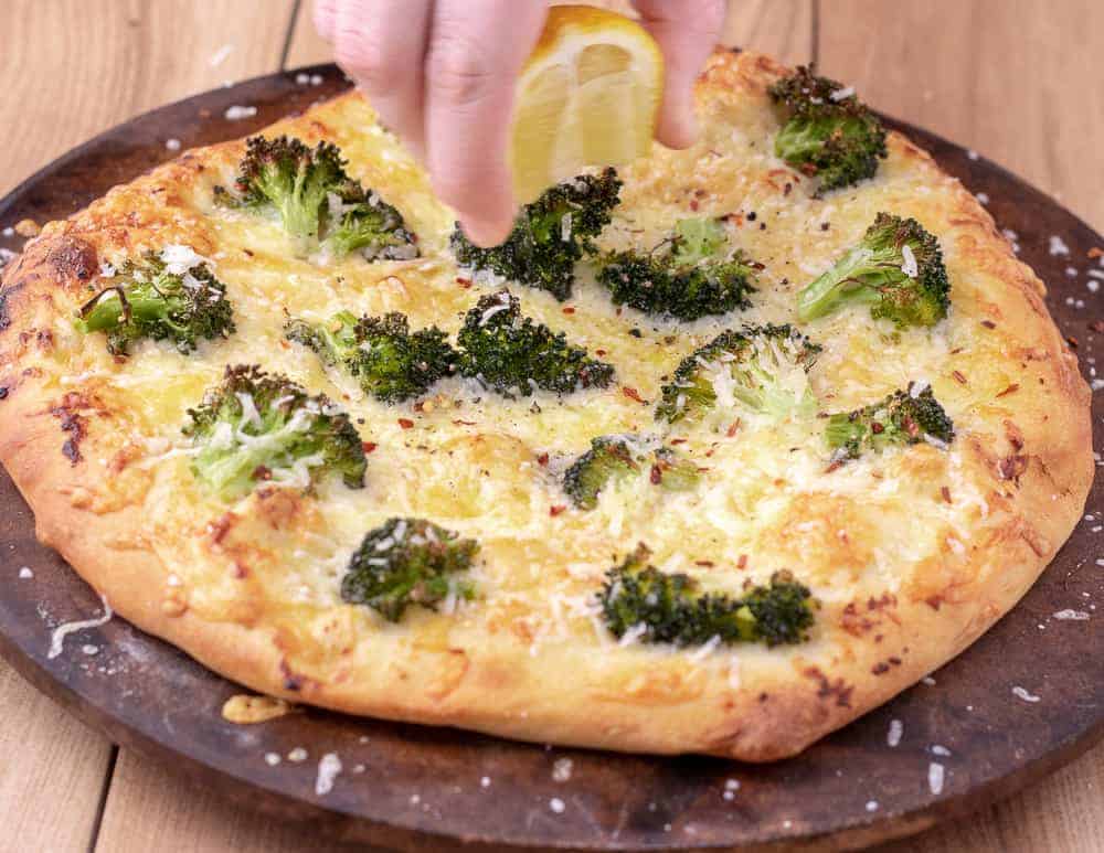 Squeezing lemon over the lemon and broccoli pizza