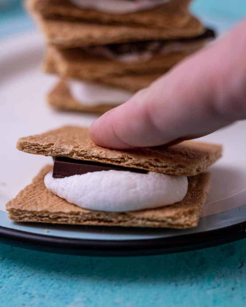 A hand smooshing a s'more on a plate