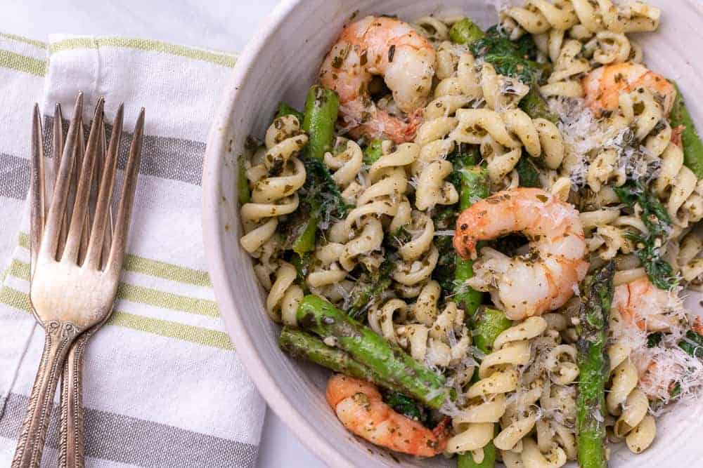 A white bowl of lemon pesto pasta with shrimp next to a fork