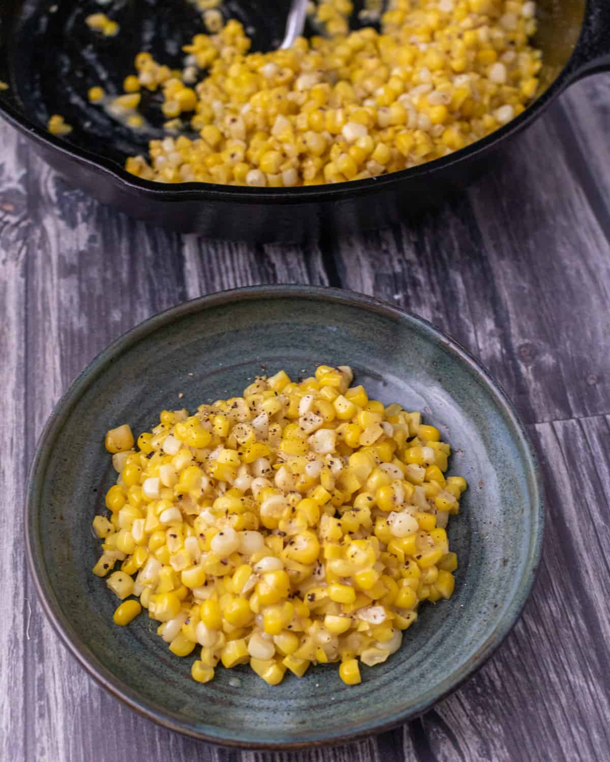 Miso butter corn on a small green plate in front of the cast iron skillet