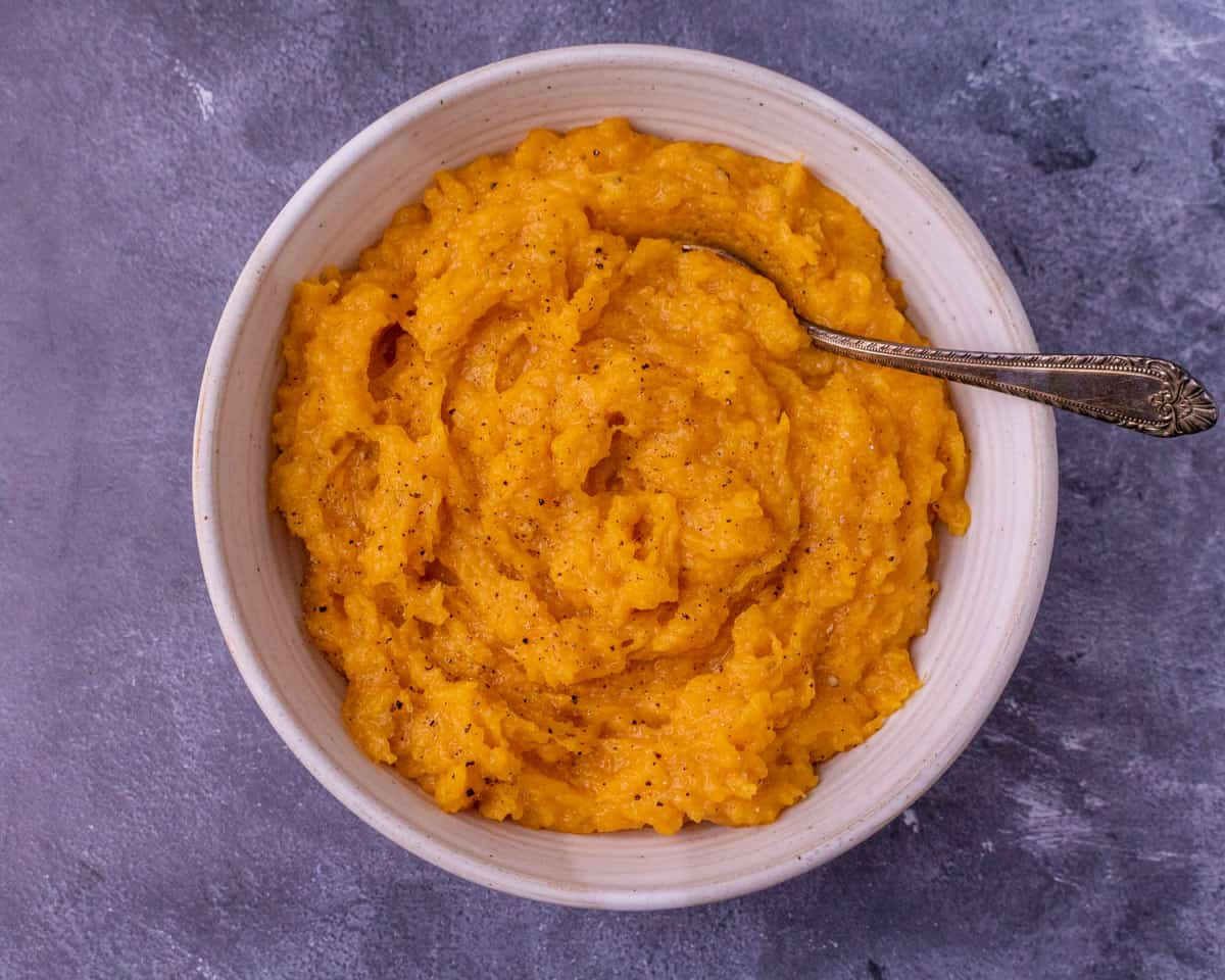 A white bowl of mashed buttter nut squash on a blue background