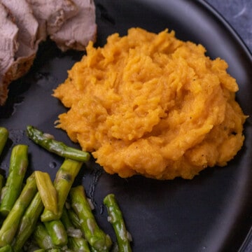 Mashed butternut squash on a plate with pork and asparagus