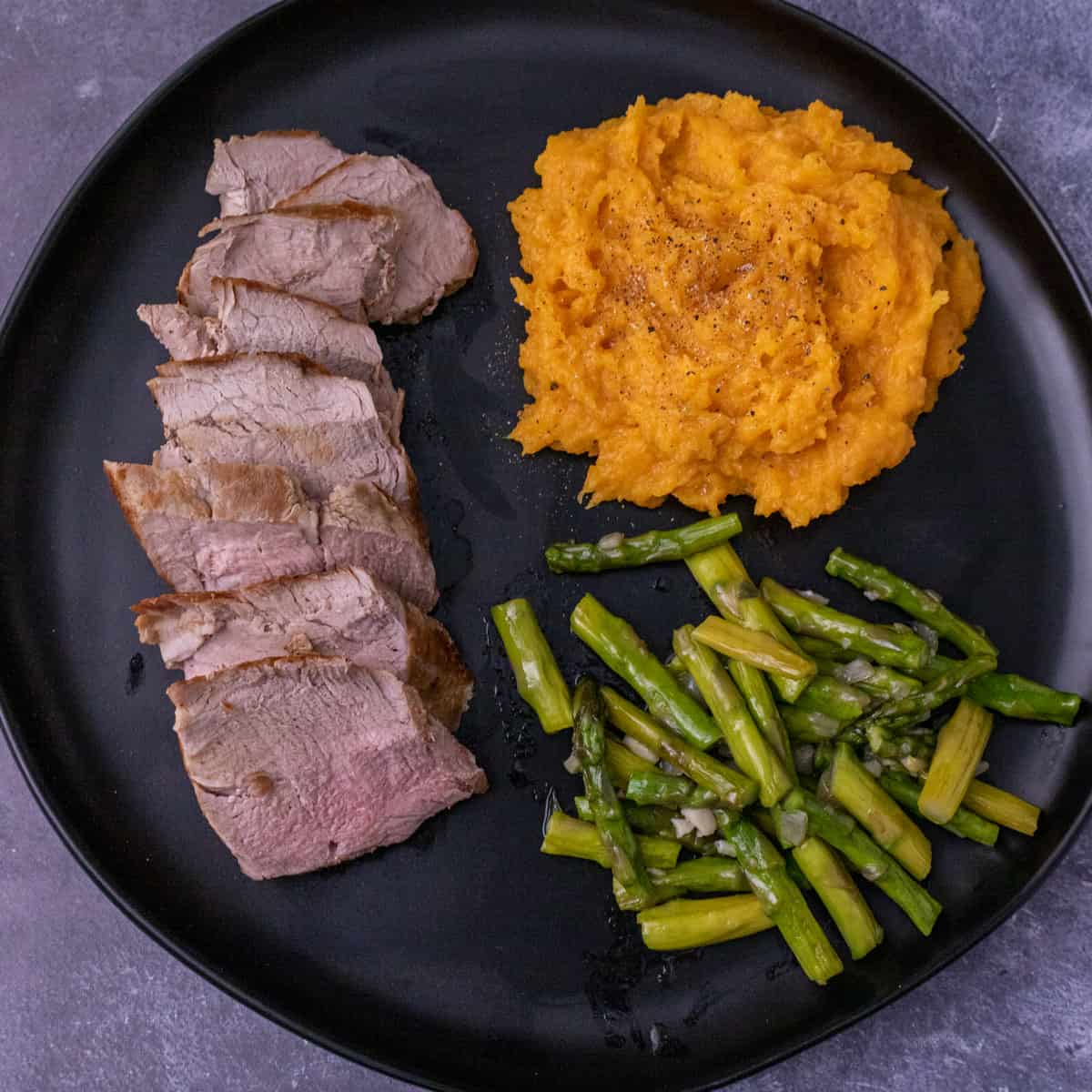 Black plate with pork tenderloin, butternut squash and asparagus