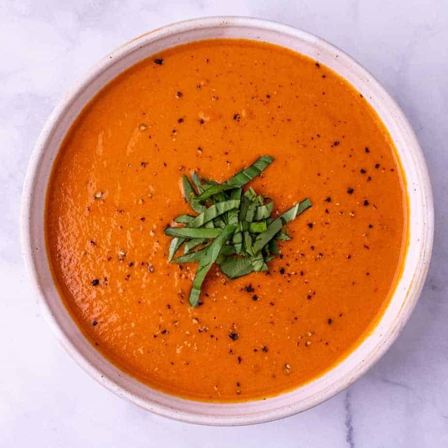 A single white bowl of tomato bisque garnished with fresh basil on a white background.