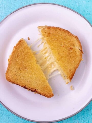 A diagonally cut grilled cheese, pulled slightly apart to show cheese pull on a white plate.