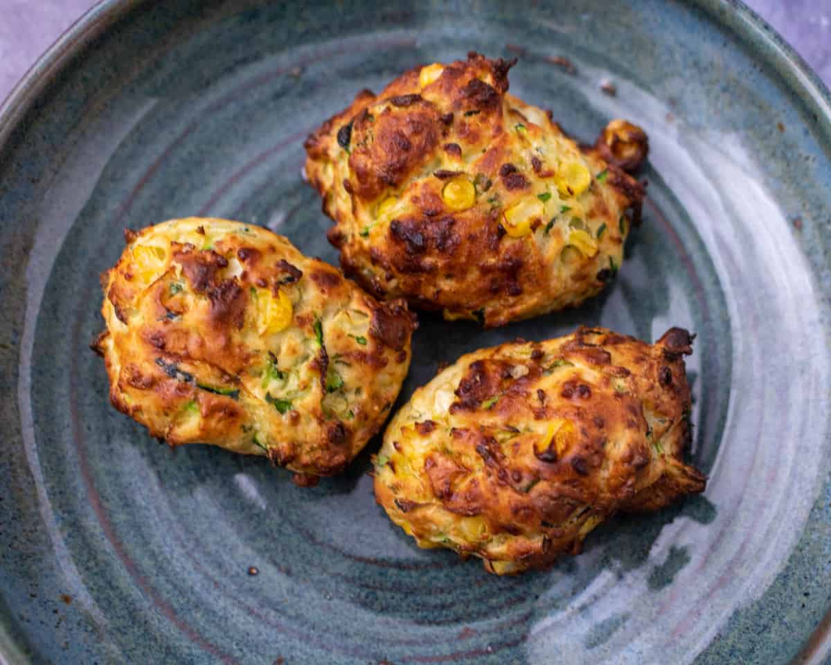 A close up of 3 fritters on a teal plate.