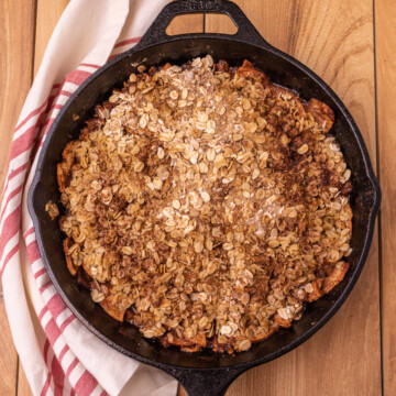 Baked apple crisp in a cast iron skillet with a red and white napkin